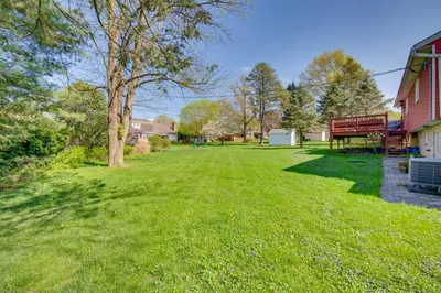 a grassy yard next to a red building with a tree at 10 Mi to Dtwn Lancaster Charming Home with Yard! in Leola