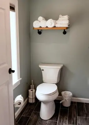 a bathroom with a toilet and a shelf with towels at Valley View Cabin in Morris