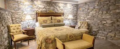 a bedroom with a stone wall with a bed and two chairs at Cameron Estate Inn in Mount Joy