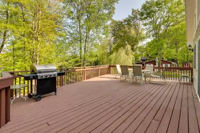 a wooden deck with a grill and chairs on it at Huge Deck Stunning Pocono Lake Vacation Rental! in Pocono Lake