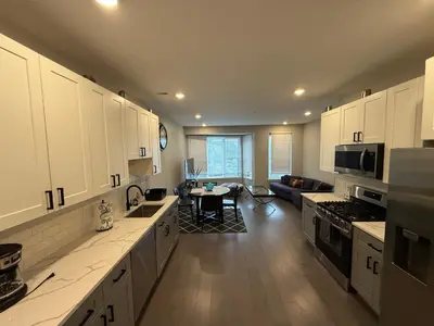 a kitchen with white cabinets and a living room at Modern 2BR 2BA Apartment with rooftop in Brewerytown in Philadelphia