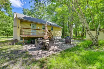 a patio with a table and chairs in front of a yellow house at Pet-Friendly Pocono Lake Cabin with Community Pool! in Pocono Lake