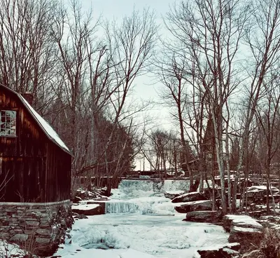 a barn with snow on the ground next to a waterfall at Lakefront Sunsets, Hot Tub, Pool Table, Kayaks in Lake Ariel