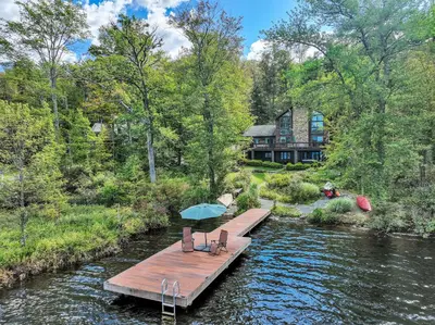 a wooden dock with two chairs and an umbrella on a river at Lakefront Sunsets, Hot Tub, Pool Table, Kayaks in Lake Ariel