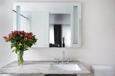 a bathroom with a sink and a mirror and a vase of flowers at Beautiful 2BD Apartment near Times Square in New York