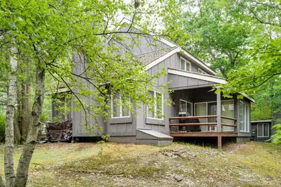 a gray house with a porch in the woods at Lake Harmony Home with Screened Porch and Hot Tub! in Lake Harmony