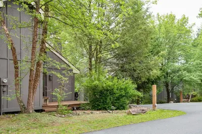 a house with a bench and trees in front of it at Lake Harmony Home with Screened Porch and Hot Tub! in Lake Harmony
