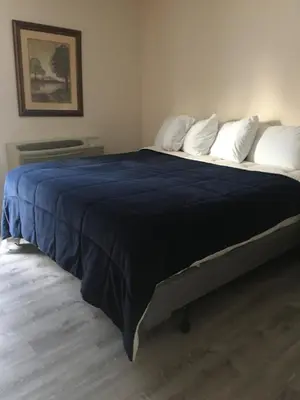 a large bed with a blue blanket and white pillows at All Suites Inn Budget Host in Lewisburg