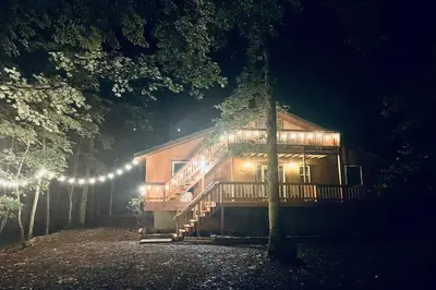 a cabin in the woods at night with lights at Pocono Chalet - Hot Tub - Game Room in Albrightsville