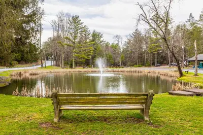 a park bench in front of a pond with a fountain at Sauna, Fire Pit Spacious and Serene Poconos Getaway in Canadensis