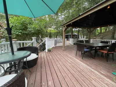 a wooden deck with tables and chairs and an umbrella at 3 Acre Lake Paradise Swimming Pool & Jacuzzi HotTub! in Hopatcong