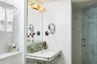a white bathroom with a sink and a mirror at The Fifth Avenue Hotel in New York