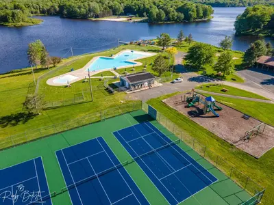 an overhead view of a pool and tennis court with a lake at The Oasis at Arrowhead in Arrowhead Lake