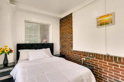 a white bed in a room with a brick wall at Chic Newark Vacation Rental 3 Mi to Airport! in Newark