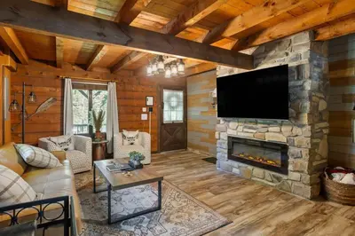 a living room with a stone fireplace with a flat screen tv at Rustic Luxury in the Pocono Mountains - Stag Lodge in Pocono Lake