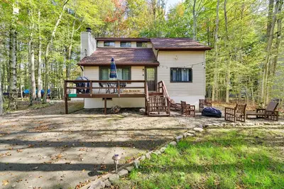 a house in the woods with a porch and chairs at Hike, Swim, Ski and More Home in Arrowhead Lakes! in Pocono Lake