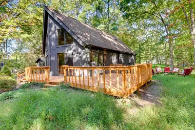 a cabin in the woods with a deck and chairs at Community Beach Access Modern Poconos Cabin! in Albrightsville