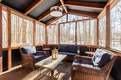 a screened in porch with wicker chairs and a table at Cozy Cabin at Poconos With Hot Tub and Fire Pit in East Stroudsburg