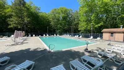 a swimming pool with lounge chairs and a group at Cozy Cabin at Poconos With Hot Tub and Fire Pit in East Stroudsburg