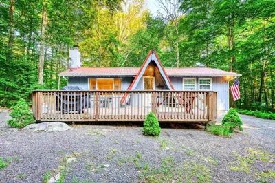 a small house with a deck in the woods at Hot Tub Fire Pit Dog Friendly in Pocono Lake