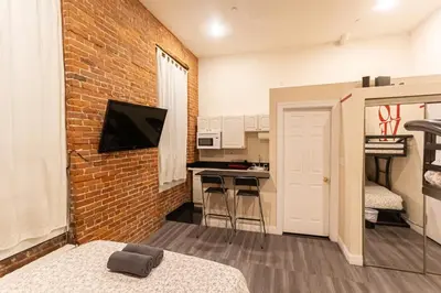 a bedroom with a brick wall and a kitchen with a counter at STUDIOPLUS by JGSTAY, Midtown ESB in New York