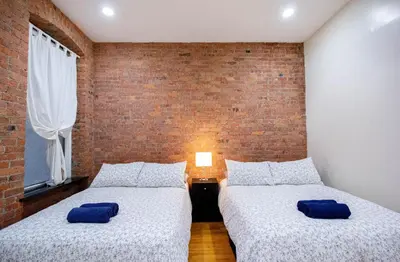 two beds in a room with a brick wall at STUDIOPLUS by JGSTAY, Midtown ESB in New York