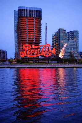 a large neon cola sign in front of a city at Room in a 2 Bedrooms apt. 10 minutes to Time Square! in West New York