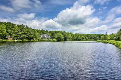 a large lake with a house in the middle at Fire Pit Arrowhead Lake Vacation Rental! in Pocono Lake