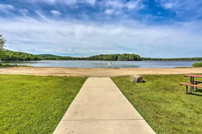 a picnic table sitting on the grass next to a lake at Fire Pit Arrowhead Lake Vacation Rental! in Pocono Lake