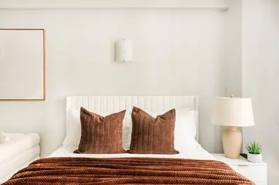 a white bedroom with a bed with brown pillows at 73-1004 New Studio UWS Doorman Gym in New York