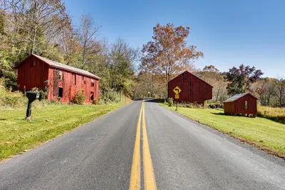an empty road with two red barns on the side at Tranquil Mt Pleasant Mills Retreat on 60-Acre Farm in Dalmatia