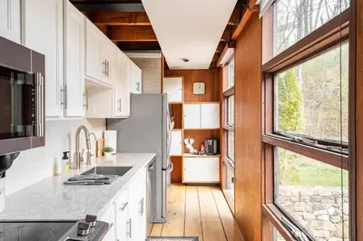 a kitchen with white cabinets and a large window at Mid Century Modern Getaway with outdoor Hot Tub in Wernersville