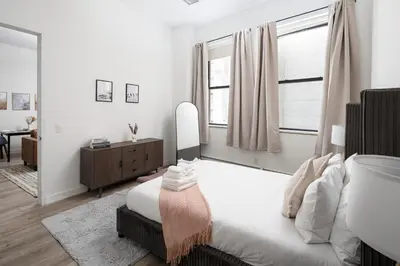 a white bedroom with a bed and a mirror at Chic 1BD with Rooftop W/D in Unit Downtown in New York