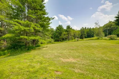 a large grass field with trees in the background at Fire Pit and On-Site Pond Wooded Walton Home! in Walton