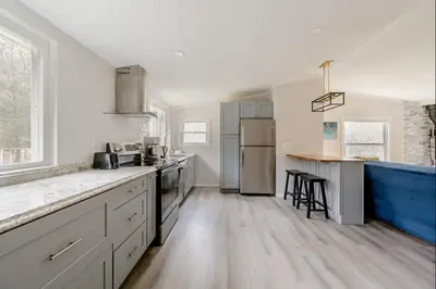a kitchen with white cabinets and a blue island at EV Serene Modern Cozy Waterfront Fireplace Cottage in Livingston Manor