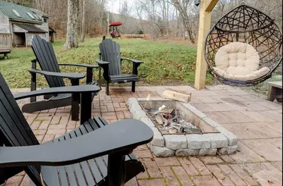 a patio with three chairs and a fire pit at EV Serene Modern Cozy Waterfront Fireplace Cottage in Livingston Manor