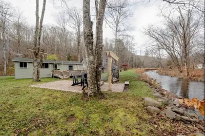 a house with a picnic table next to a river at EV Serene Modern Cozy Waterfront Fireplace Cottage in Livingston Manor