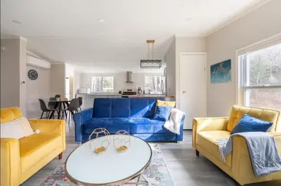 a living room with a blue couch and yellow chairs at EV Serene Modern Cozy Waterfront Fireplace Cottage in Livingston Manor