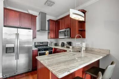 a kitchen with wooden cabinets and a stainless steel refrigerator at XL Studio - Modern Studio with Rooftop Pool in Philadelphia