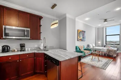 a kitchen with wooden cabinets and a living room at XL Studio - Modern Studio with Rooftop Pool in Philadelphia