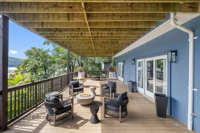 a deck with chairs and tables on a blue house at Lakeview Villa with Private Hot Tub, Firepit & Spacious Decks with Breathtaking Cliff Views in Greenwood Lake