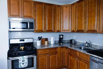 a kitchen with wooden cabinets and a stove and microwave at Rainforest Retreat 20m to NYC Parking Sleeps 25 in Bayonne