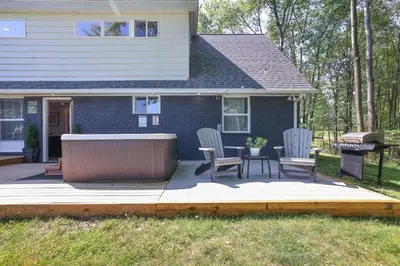 a patio with two chairs and a grill in front of a house at POCONOS BRAND NEW LAKEFRONT Oasis 1 ACRE, HOTTUB GAMEROOM FIREPITS TALK ABOUT PRIVACY in Albrightsville