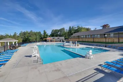 a large swimming pool with blue chairs and a building at Fire Pit, Pool and Beach Access Tobyhanna Home! in Tobyhanna