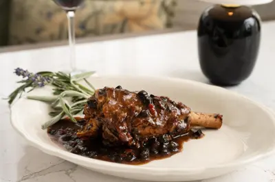 a white plate with meat and beans and a glass of wine at Pendry Natirar in Peapack