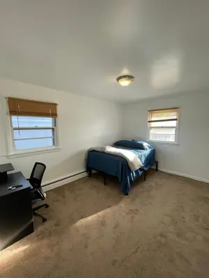 a bedroom with a bed and a desk and two windows at Cozy Home Near Downtown Rahway in Rahway