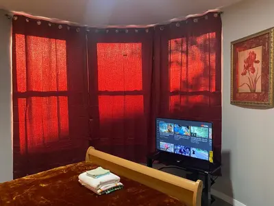 a bedroom with red curtains and a bed and a tv at Cozy Getaway Room in Newark