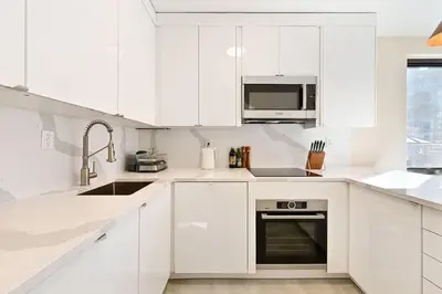 a white kitchen with white cabinets and a sink at Modern one bedroom with private balcony in New York