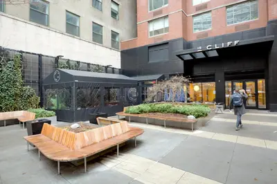 a woman walking in front of a building with benches at FiDi 2br w wd doorman elevator roof NYC-772 in New York