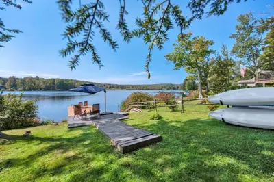 a dock with a table and chairs on the grass next to a lake at Lakeside, Dock, Hot Tub, Kayaks, Arcade, Playset in Lake Ariel